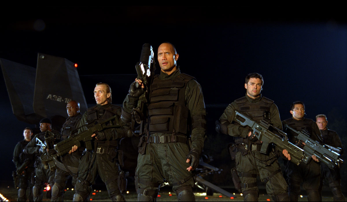 the rock and karl urban (along with other actors) pose in tactical gear with huge weapons